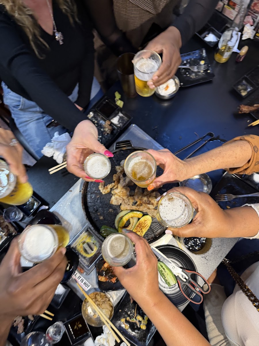 Friends raising glasses over a Korean BBQ grill at J BBQ